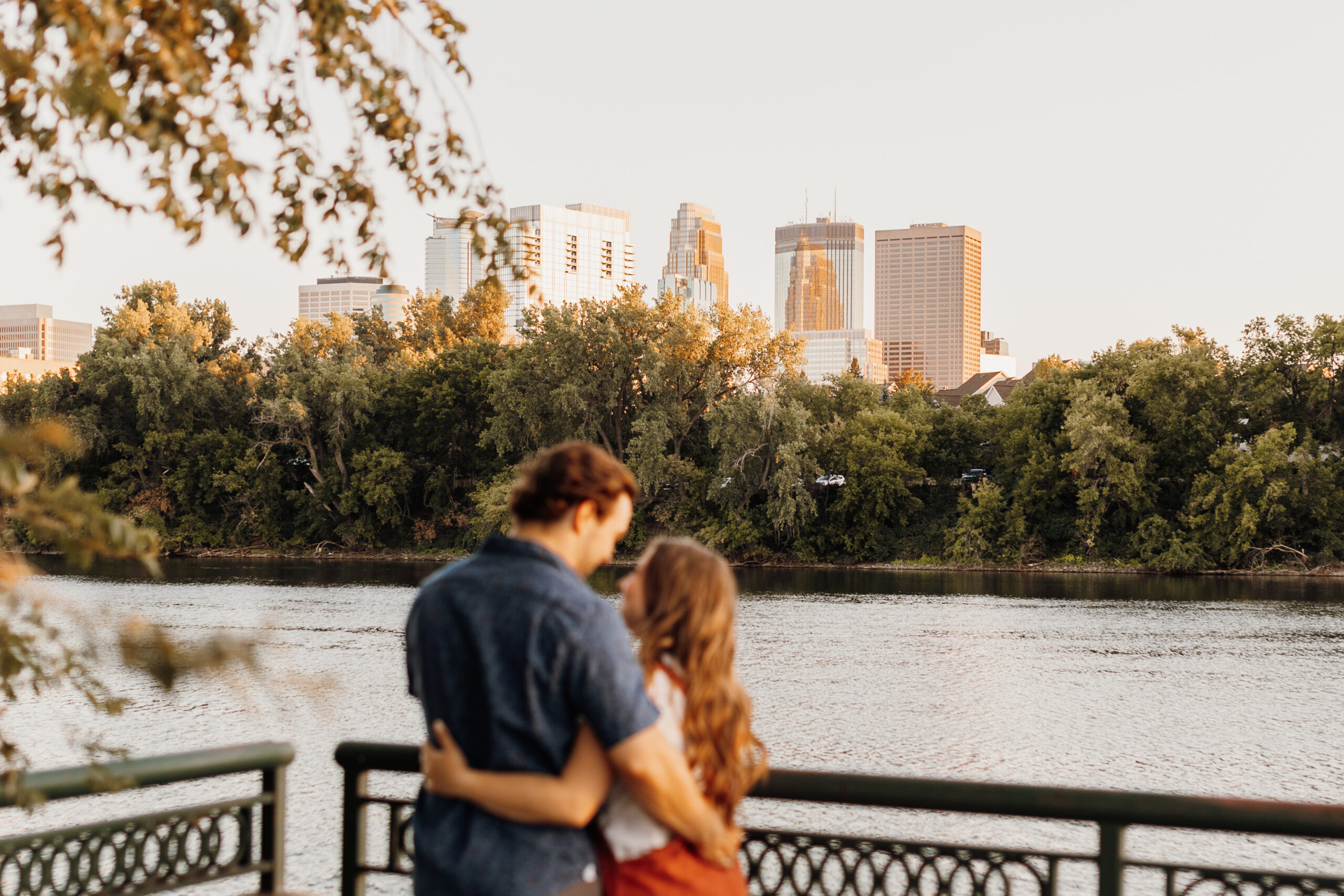 couple holding each other while looking at the Mississippi river and Minneapolis skyline at boom island park